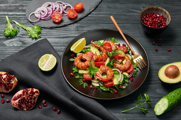 Shrimps salad, avocado, lettuce, cherry tomatoes. Home made vegetarian shrimp salad. Seafood concept. Tasty veg mixed leaves, grilled prawn shrimps in plate on black wood background.