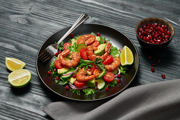 Shrimps salad, avocado, lettuce, cherry tomatoes. Home made vegetarian shrimp salad. Seafood concept. Tasty veg mixed leaves, grilled prawn shrimps in plate on black wood background.