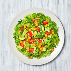 Vegan greens salad, chickpeas, lettuce, arugula, cherry tomatoes. Home made vegetarian green salad. Diet, vitamin food concept on wood. Tasty veg mix leaves salad in bowl. Top view.