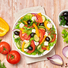 Greek salad with cucumeber, olives, feta cheese, cherry tomatoes, bell pepper, onion and lettuce. Diet, vitamin food. Healthy vegetarian meal concept. Tasty salad in bowl on wood, top view.