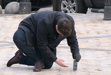 A young man tourist on his knee makes a photo on his cell phone