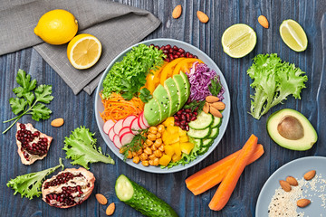Buddha bowl salad with avocado, tomato, lettuce, cucumber, red cabbage, chickpeas, pomegranate. Paleo diet, healthy vegan and balanced food concept. Fresh rainbow mix green salad on wood