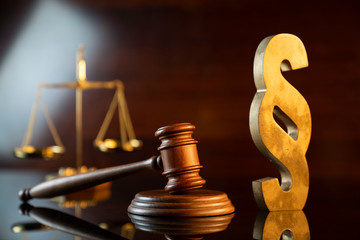 Law and justice concept. Judge’s gavel, scale and paragraph sign on the shining wooden brown table and the brown background.