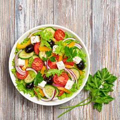 Greek salad with cucumeber, olives, feta cheese, cherry tomatoes, bell pepper, onion and lettuce. Diet, vitamin food. Healthy vegetarian meal concept. Tasty salad in bowl on wood, top view.