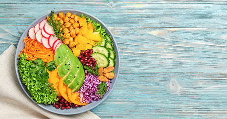 Buddha bowl salad with avocado, tomato, lettuce, cucumber, red cabbage, chickpeas, pomegranate. Paleo diet, healthy vegan and balanced food concept. Fresh rainbow mix green salad on blue wood