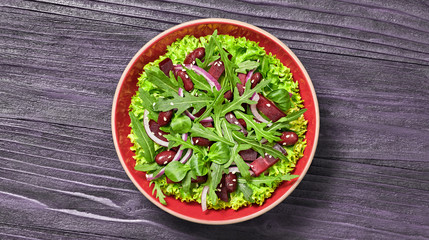 Vegan beetroot salad with red bean, lettuce, arugula, sunflower, sesame seed. Home made vegetarian beet max leaves salad on wood background. Tasty fresh beetroot diet vegan dish. Top view.