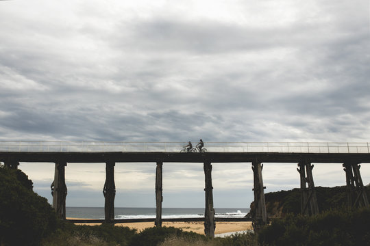 silhouette photos of bicycle riders on Kilcunda Bourne Creek Trestle Bridge on an overcast day in Gippsland Victoria with the sea in the background