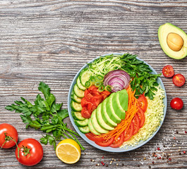 Fresh salad with avocado, lettuce, cucumber, cabbage, carrot, onion. Diet, healthy vegan salad, balanced food concept. Buddha bowl mix vegetable homemade salad on wood, top view.
