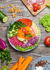 Rainbow salad with tomato, lettuce, cucumber, red cabbage, carrot, radish. Paleo diet, healthy vegan and balanced food concept. Fresh mix green leaves homemade vegetable salad on wood, top view