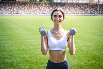 Beautiful woman with dumbbells making morning exercises outdoor. Sport and health concept