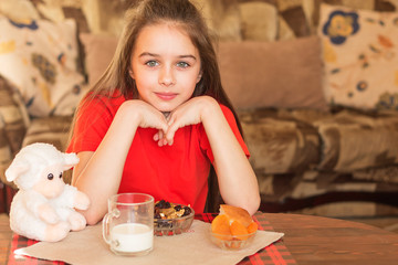 Attractive girl in a red T-shirt is sitting at home at the table at the morning breakfast.