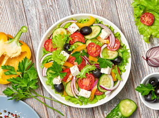 Greek salad with cucumeber, olives, feta cheese, cherry tomatoes, bell pepper, onion and lettuce. Diet, vitamin food. Healthy vegetarian meal concept. Tasty salad in bowl on wood, top view.