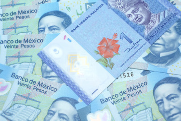 Fototapeta premium A close up image of a blue one Malaysian ringgit bank note on a bed of Mexican twenty peso bank notes close up in macro