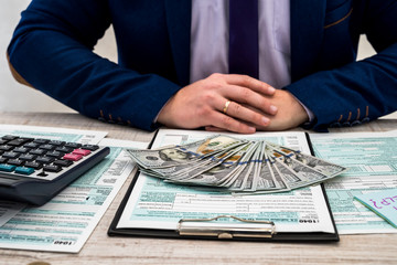 A businessman fills out an individual 1040 tax form and counts dollars. Male hands writing on paper...