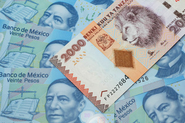 A close up image of a two thousand Tanzanian shilling bank note on a background of Mexican twenty peso bank notes