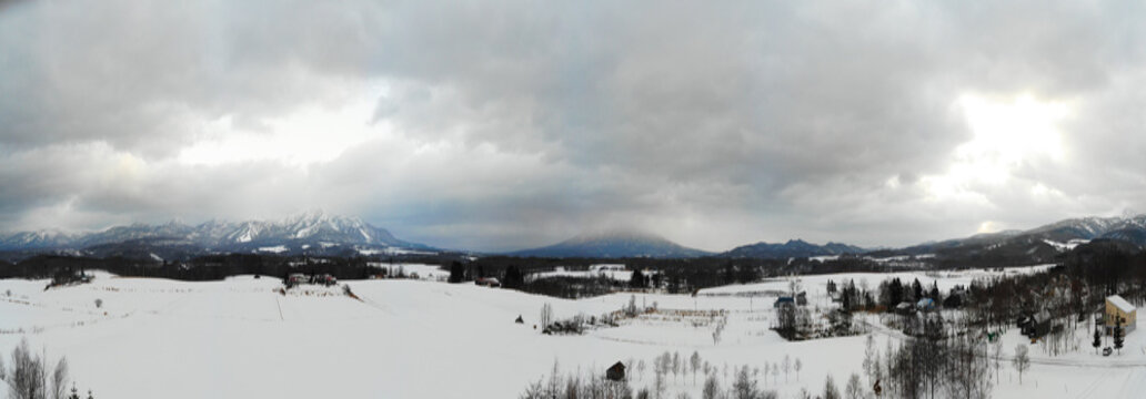 Panoramic Winter landscape photo of snow covered fields and bare trees with the majestic Mount Yotei in the background 