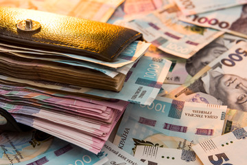 The thick money-laden black men's wallet lies against the backdrop of Ukrainian hryvnia money.