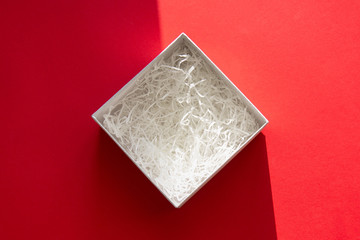 open box with filling material inside lying on a red colored paper background with shadow, top view