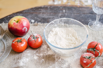 Wooden table decorated with, a canvas tablecloth and glassware on the table flour, tomatoes, cucumbers and apples.