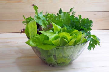 Vegan healthy food - lettuce, parsley, celery leaves in a transparent cup on a wooden table.