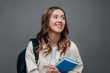 Happy girl student laughs and smiles and looking away holding a notebook isolated over grey background, copy space. Happy freelancer girl