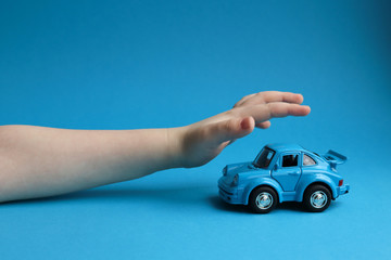 Blue toy car on a blue background and a children's hand that wants to take it