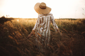Woman in linen dress and hat walking in wildflowers and herbs in sunset golden light in summer...