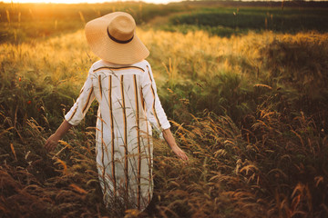 Woman in linen dress and hat walking in wildflowers and herbs in sunset golden light in summer...