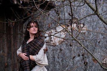 Portrait of a woman near the wall of an old house with tree branches. Girl in vintage clothes, gloomy photo for Halloween, copy space for text