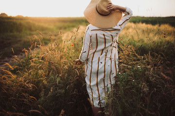 Woman in rustic dress and hat walking in wildflowers and herbs in sunset golden light in summer...
