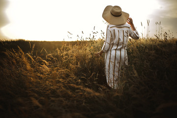 Woman in linen dress and hat walking in wildflowers and herbs in sunset golden light in summer...