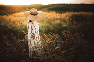 Woman in rustic dress and hat walking in wildflowers and herbs in sunset golden light in summer...