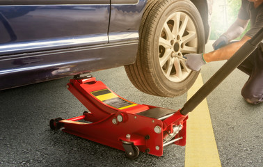 Red hydraulic  floor jack ,Asia man with a blue car that broke down on the road.Changing tire on...