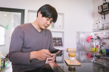 Attractive Asian man using smartphone to take coffee photos at the table in coffee shop. Film tone effected.