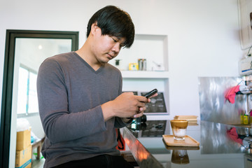 Attractive Asian man using smartphone to take coffee photos at the table in coffee shop. Film tone effected.