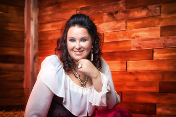 Portrait of fat plump fun charming cute woman with black curly hair in the room with hay and straw