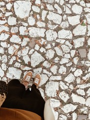 Flat lay, top view. Young woman standing on the  stone road. Legs in sneakers.