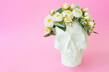 Plaster skull with white flower crown on pink background