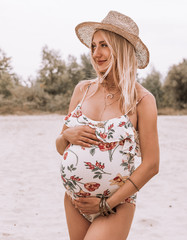 Young happy pregnant woman in a swimsuit and hat on the sandy beach . pregnancy concept