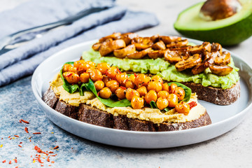 Vegan toasts with hummus and chickpeas,  guacamole and mushrooms on rye bread. Healthy vegan food concept.