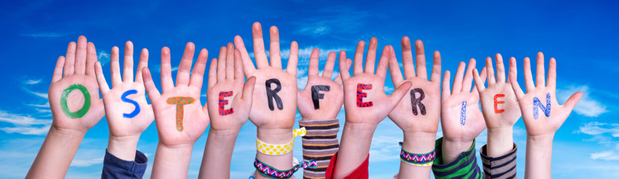 Children Hands Building Colorful German Word Osterferien Means Easter Break. Blue Sky As Background