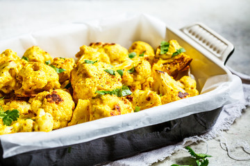 Baked cauliflower with spices and greens in black oven dish.
