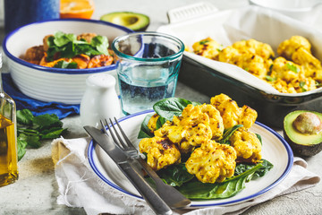 Vegetarian dining table. Baked cauliflower salad with spinach, baked vegetables, vegan meatballs and avocado.