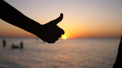 Hand giving thumbs up at sunset background on the beach
