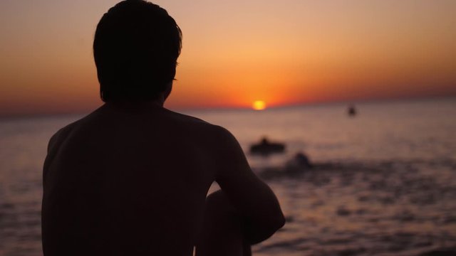 Silhouette of a man sitting alone on the beach looks sunset. Lonely, thinking person.