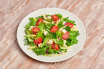 Fresh salad with cherry tomatoes, savoy cabbage, cucumeber on dish. Healthy summer salad vegetarian meal concept. Tasty mixed leaves, tomatoes and mix vegetable salad on wood background
