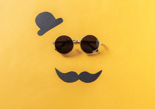Hipster sunglasses and funny moustache with hat on yellow background.flat lay, top view.