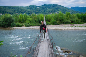 woman crosses a mountain river over wooden bridge