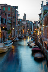 Fototapeta na wymiar Narrow canal with boats and vintage houses at dusk. Venice city at night