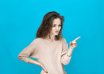 Portrait of a young beautiful woman wearing sweatshirt points and looking to the side isolated over blue background